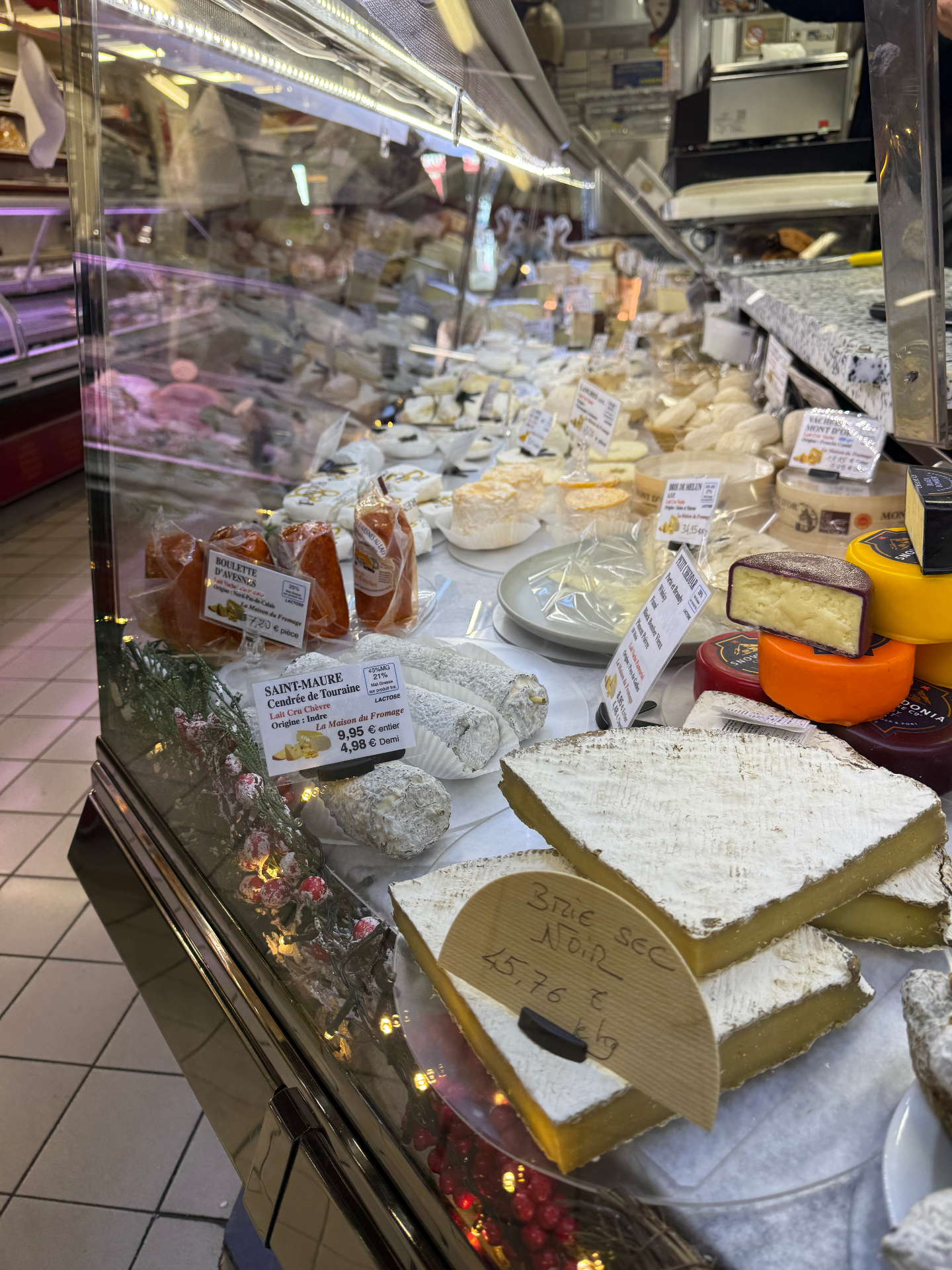 Saint-Maure de Touraine goat cheese and aged Brie on display at a traditional French market fromagerie